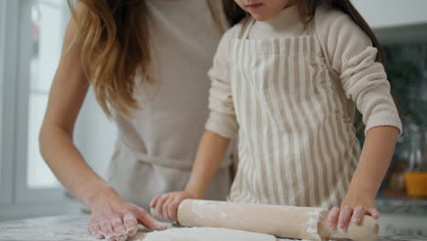 mother daughter rolling dough home close up. smiling woman teaching kid cooking