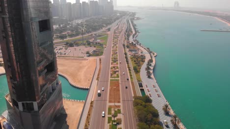 aerial tilt down shot to overhead of a freeway in abu dhabi between the skyscrapers and the water