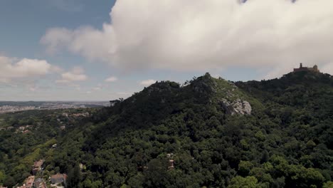 Aerial-panning-shot-of-Sintra-Hills-against-beautiful-cloudscape-and-Pena-palace-in-distance-mountaintop