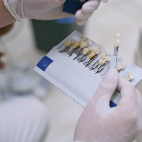 dentist holding artificial teeth. stomatologist in white sterile gloves choosing color of synthetic tooth. benefits of tooth implants.