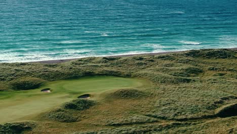 waves crashing on shoreline of coastal irish links golf course, aerial drone flyover