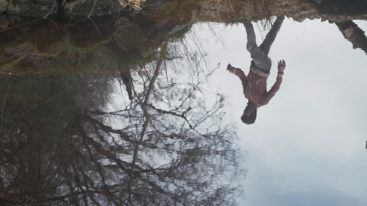 A man's reflection in the lake shoreline