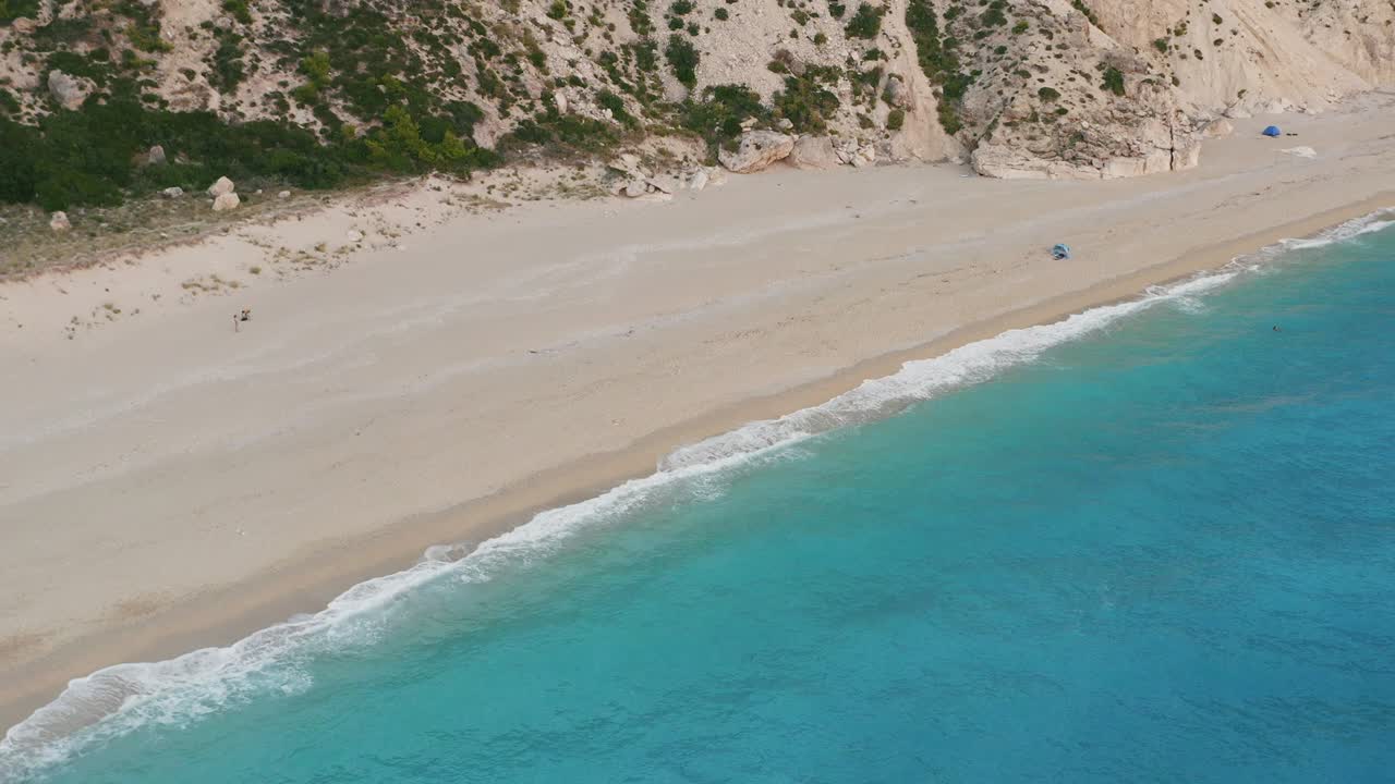 Aerial view of beautiful Milos beach of Lefkada, Ionian island, Greece. Pristine waves breaking the turquoise blue sea on the shore at sunset light