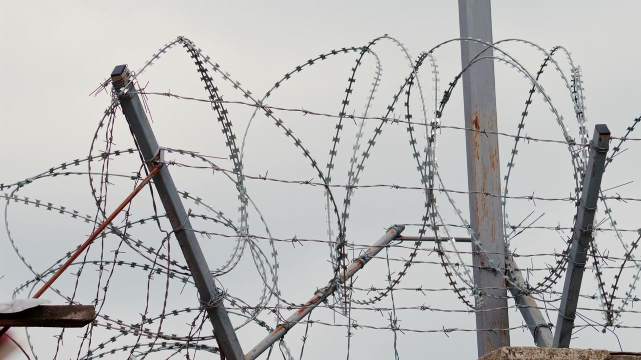 A sharp close up of barbed wire stretched across a fence, with a blurred building in the background