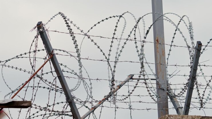 A sharp close up of barbed wire stretched across a fence, with a blurred building in the background