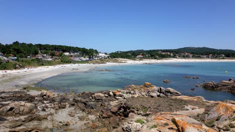 Aerial-Footage-of-Relaxing-Beach-with-Rocks-Forest-and-Buildings-in-Spain