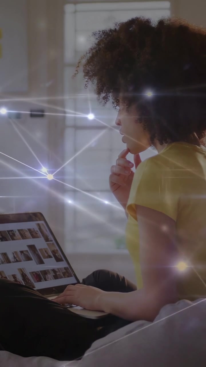 Vertical video: Woman scrolling laptop pics, causing nodes overlaying over scene, curating content