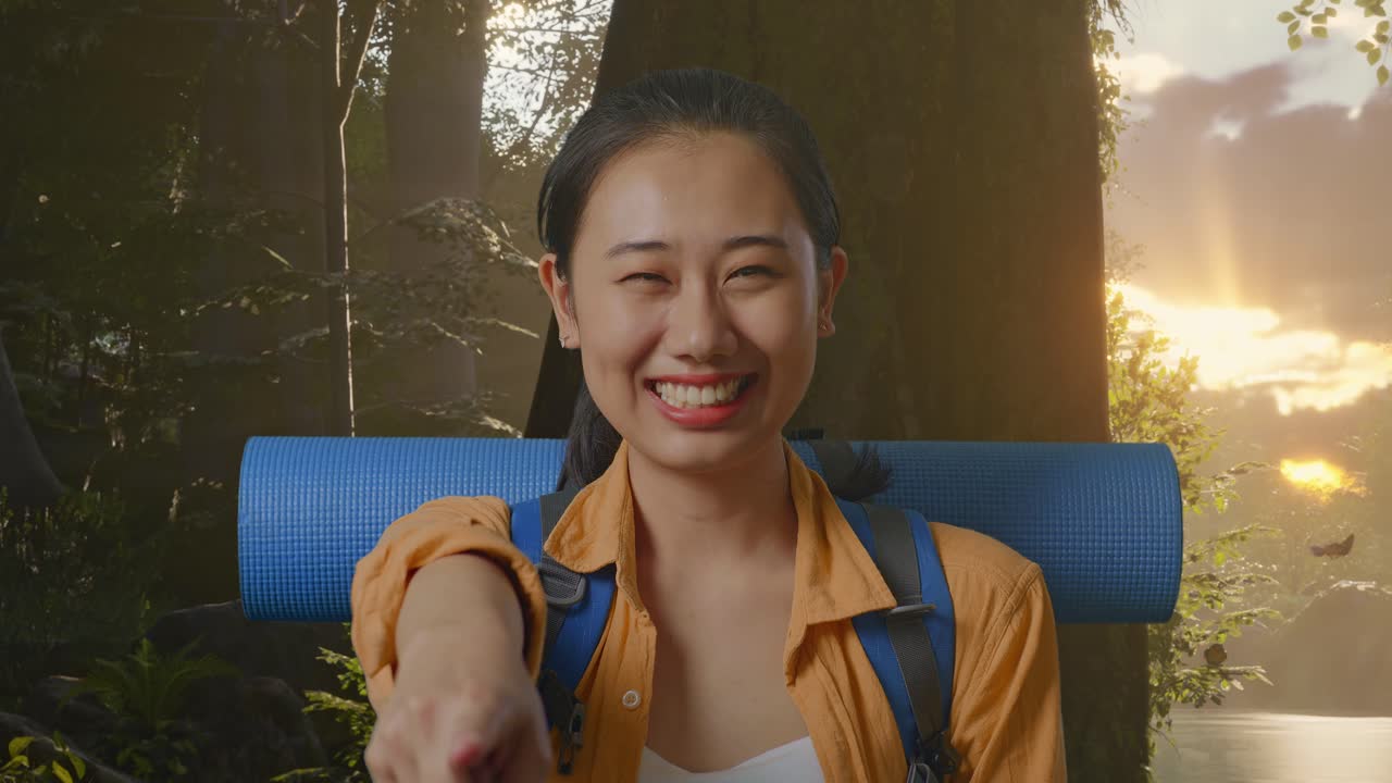 산악 배을 들고 있는 아시아 여성 하이커가 웃으며 가을 만지고 숲의 자연을 탐험하는 동안 카메라를 가리키고 있습니다.