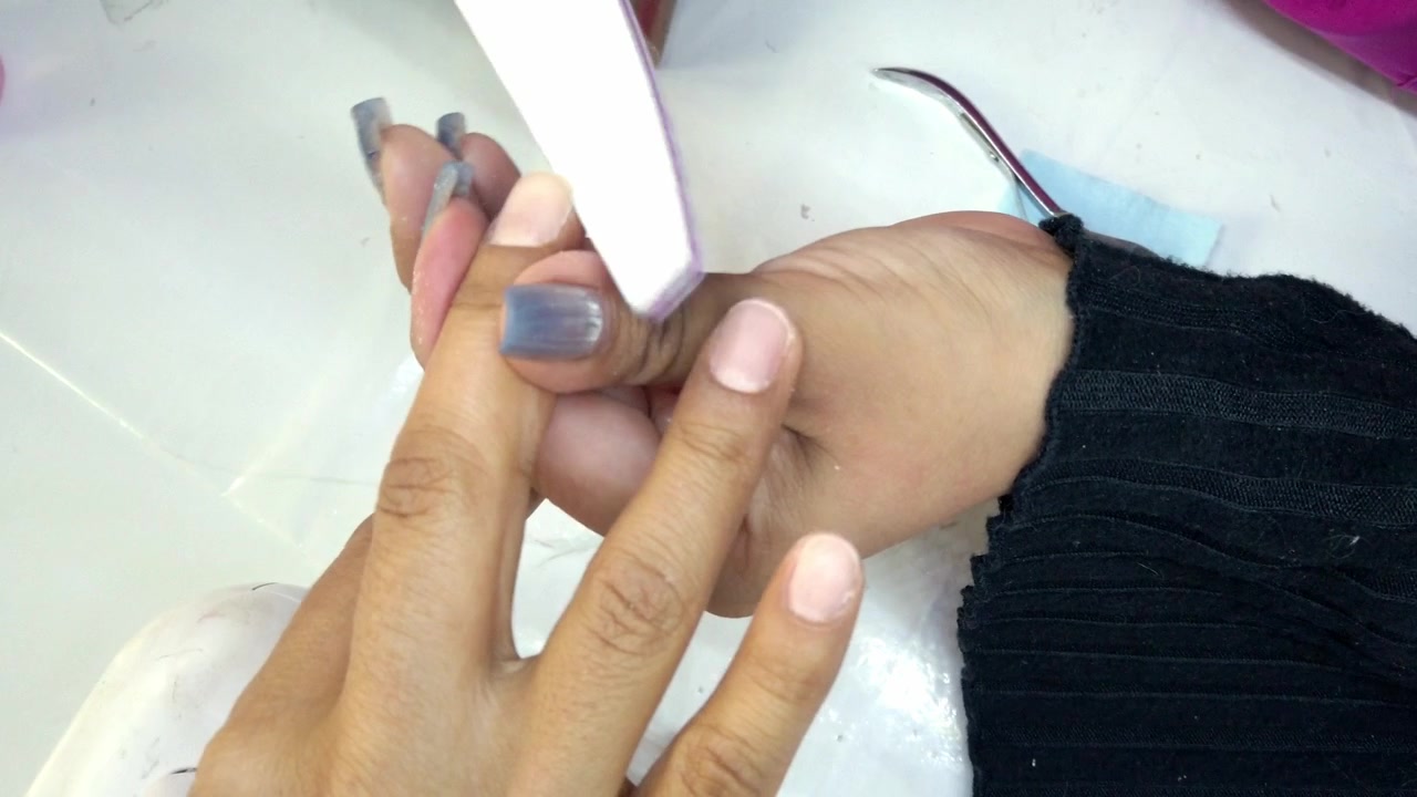 Closeup of nail technician filing fingernails during manicure session with beauty treatment cosmetic care and professional salon procedure indoors