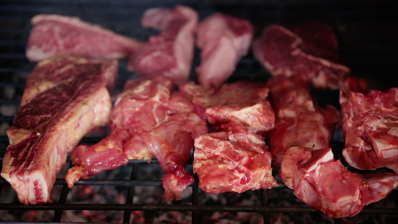 Piezas variadas de carne cruda colocadas en una parrilla sobre brasas calientes antes de cocinar
