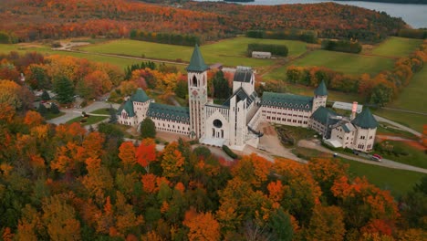 aerial shot around saint benoit du lac abbey at fall with colorful trees near magog on and memphremagog lake in quebec region, autumn season, canada