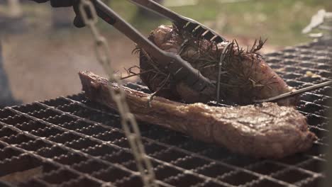 a handheld shot of grilling meat outdoors on a hanging grill