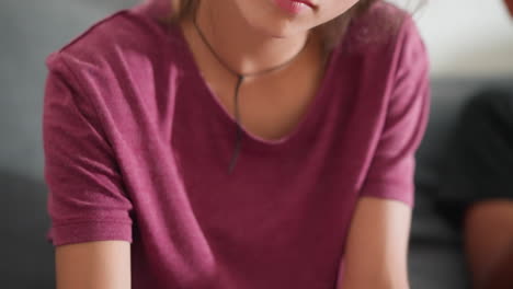 close up of cute kid in maroon top focused on writing with serious expression while blurry view of another person nearby emphasizes cozy indoor environment