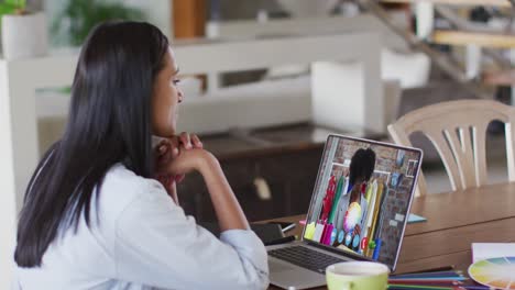 Mixed-race-businesswoman-sitting-at-table-using-laptop-having-video-call-with-female-colleague