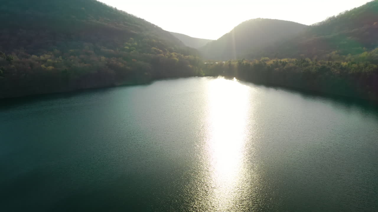 Gün batımında yeşil dağlarla çevrili bir orman gölü üzerinden sinematik havadan geri çekilme