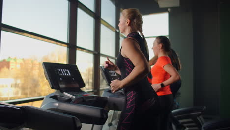 a young beautiful woman and three people running on a treadmill in a fitness room performing a cardio workout. indoor running warm-up before training in slow motion.