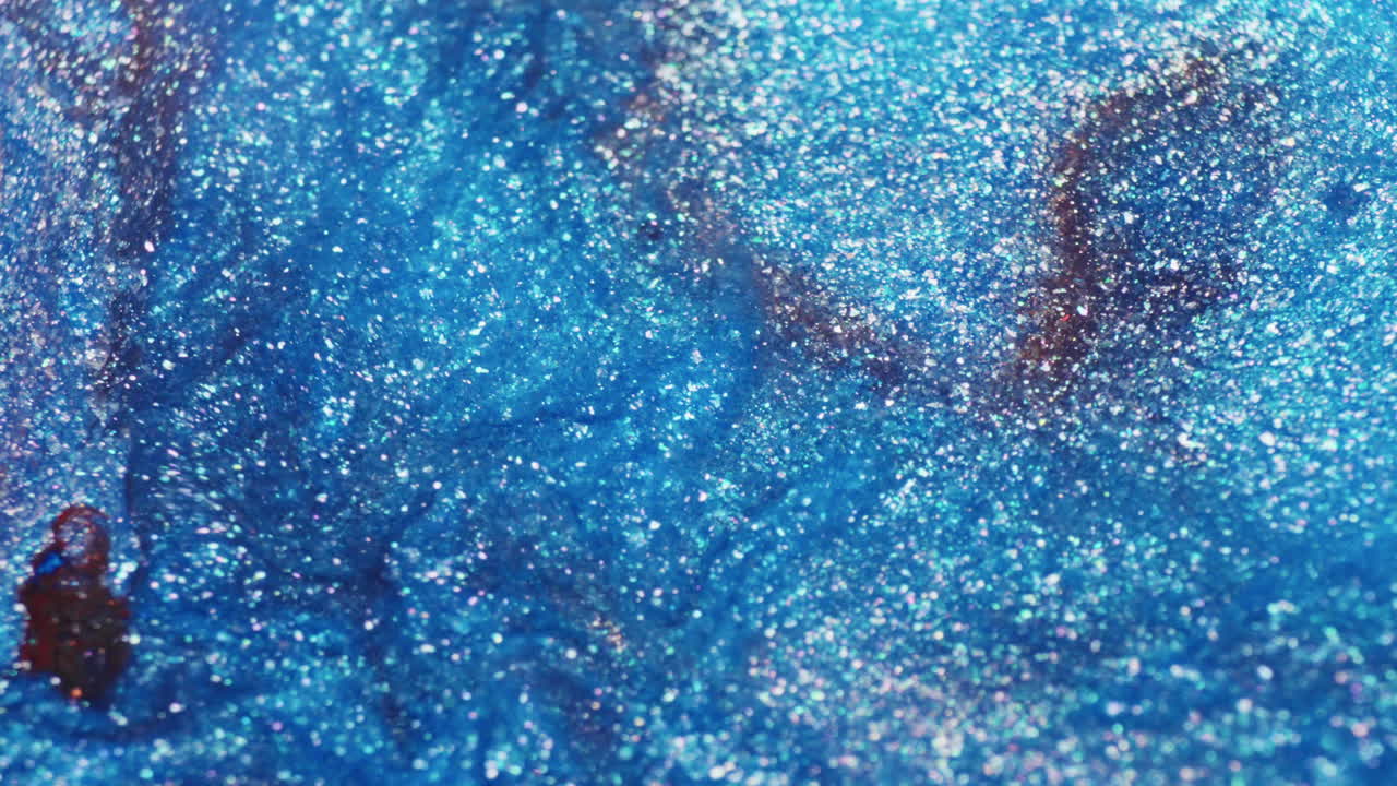 Macro shot of blue glitter ink with hints of brown, showing subtle liquid flow and shimmering surface textures