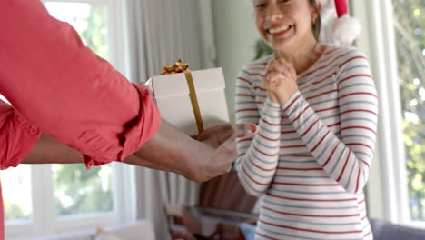 midsection of happy diverse couple exchanging christmas gift at home, slow motion