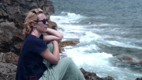 woman sitting on cliff relaxing by the sea, looking at waves, mallorca