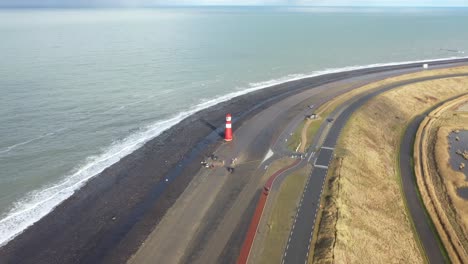 drone shot of the dutch coastline, flying forwards, with a big red lighthouse.
