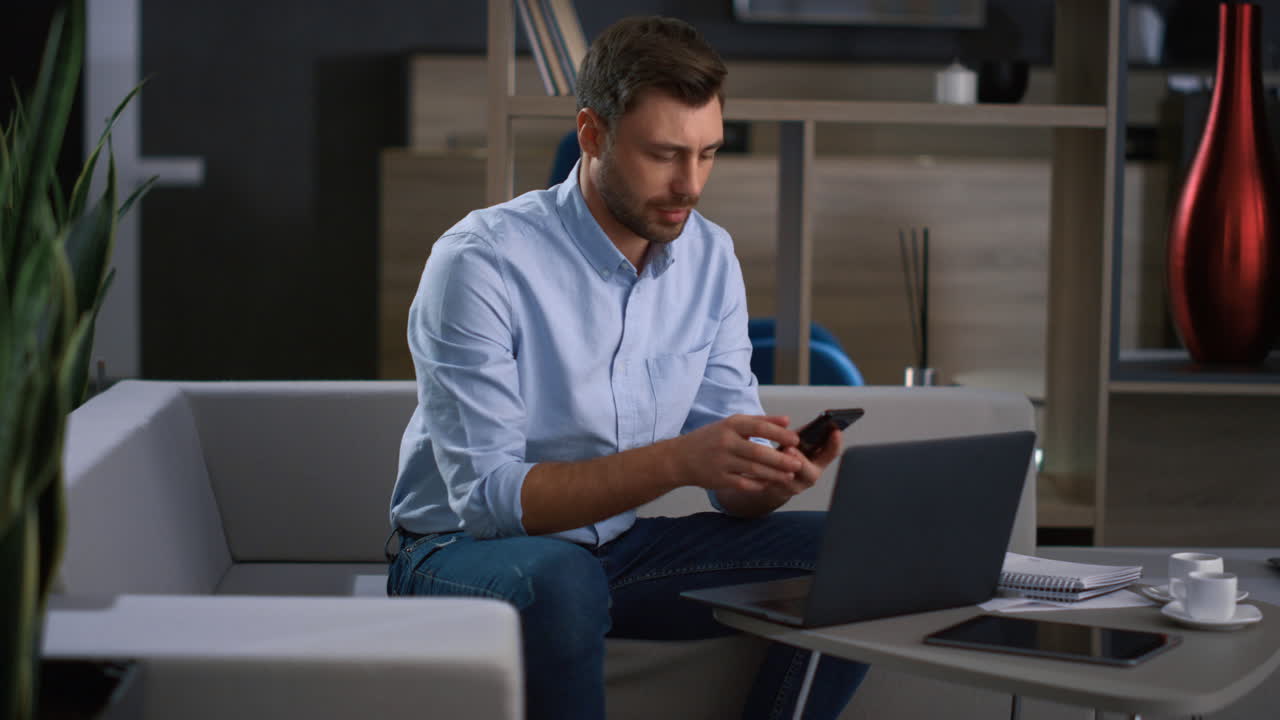 un empresario sonriente llama al móvil usando una computadora portátil para investigar datos de negocios en la oficina.