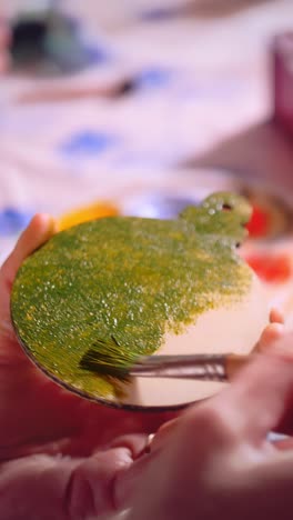 artist applying green paint with brush on round wooden surface, showcasing creativity and attention to detail in a vibrant crafting environment
