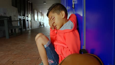 side view of asian schoolboy sitting alone with hands covering his face in school corridor 4k