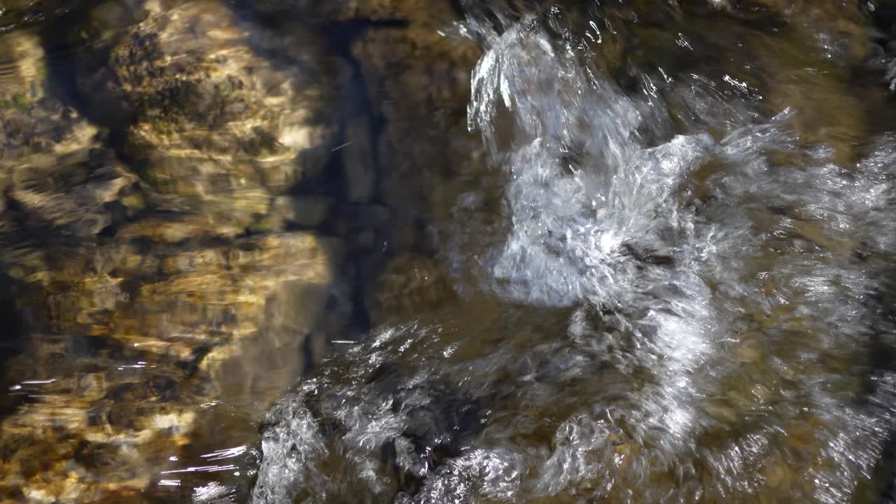 Top-down view of water flowing over rocks and stones near Walensee, Switzerland. Natural stream detail. Ideal for nature and texture backgrounds.