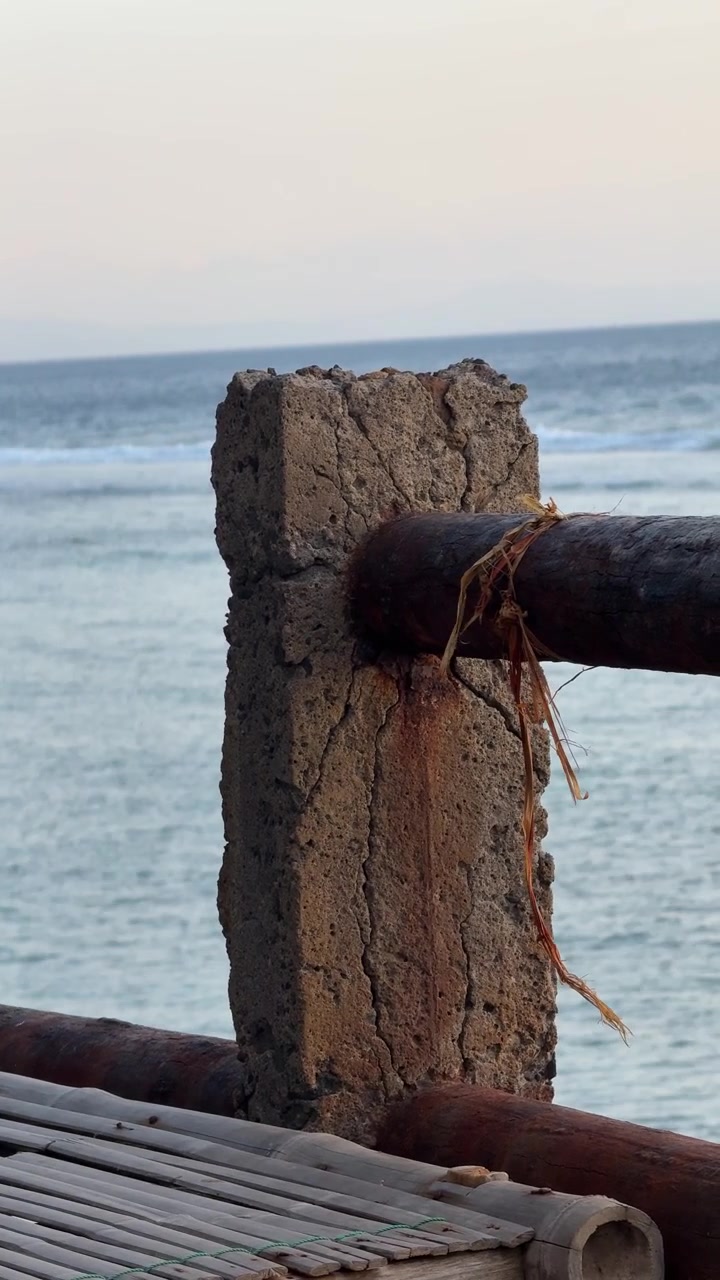 Forvitret betonpæl og trægelænder med udsigt over havet