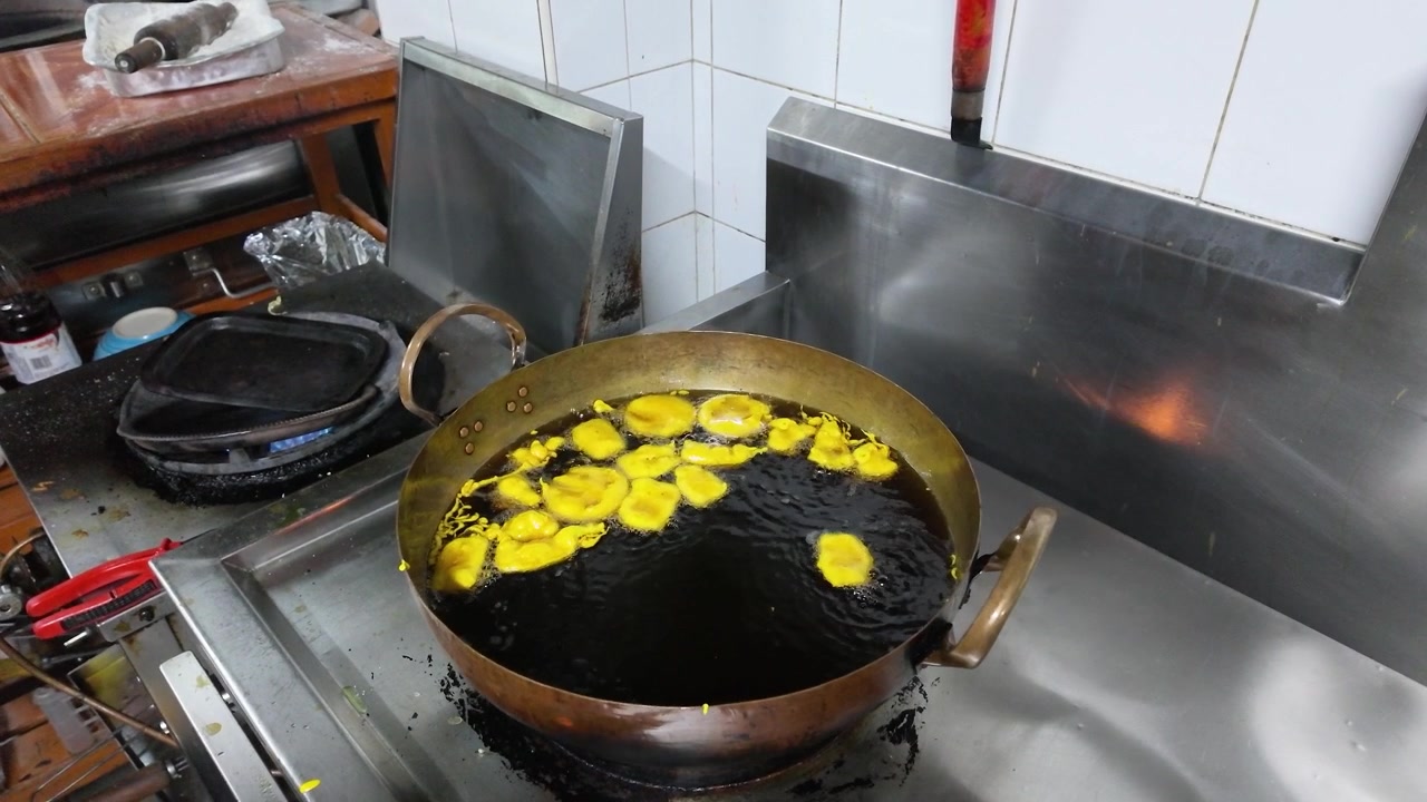 Yellow vegetable fritters sizzle in hot oil within a brass wok on a gas stove.