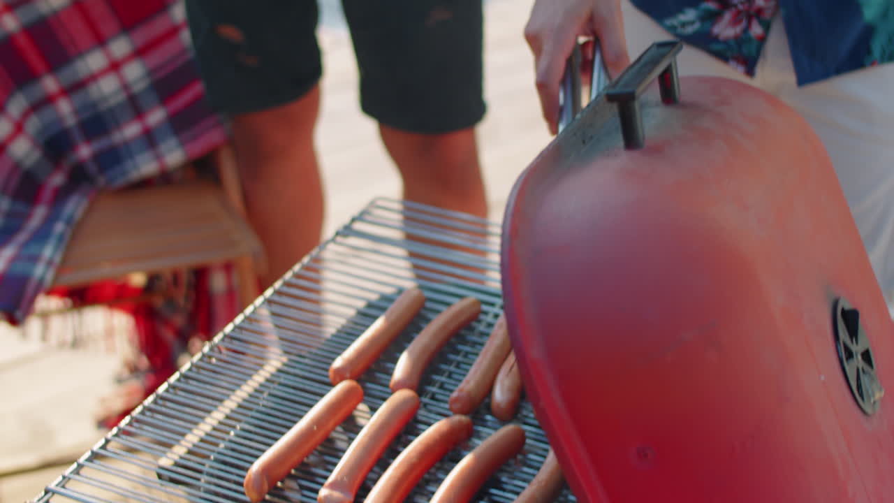 hombre cocinando salchichas a la parrilla y tomando cerveza en una fiesta al aire libre