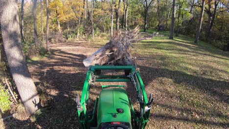 Punto-De-Vista-De-ángulo-Alto-En-Un-Pequeño-Tractor-Verde-Usando-Horquillas-Elevadoras-Para-Mover-Un-Tocón-De-árbol-A-Lo-Largo-De-Un-Camino-En-El-Bosque-En-Otoño