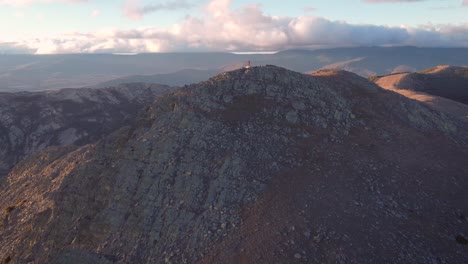 Aerial-shot-back-view-of-young-hiker-in-mountain-range-close-to-Madrid-during-afternoon-with-blue-sky-and-white-clouds