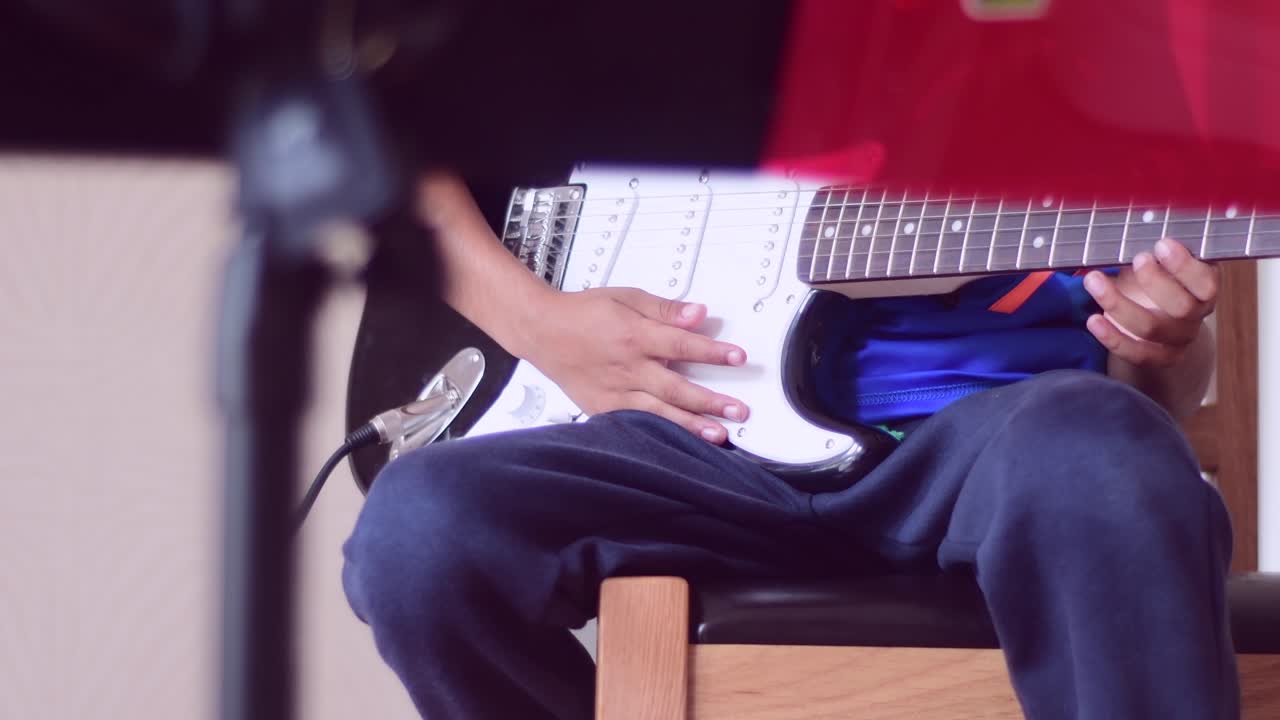 A young boy (school age) practicing on the electric guitar at home with a microphone and music stand in front.