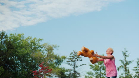 Frau-Mittleren-Alters,-Die-Spaß-Hat-Wie-Ein-Kind---Auf-Einem-Trampolin-Springen-Und-Einen-Teddybären-Hochwerfen