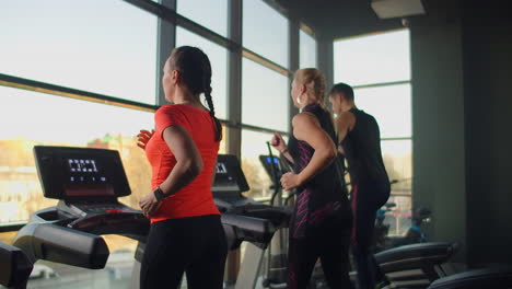 a young beautiful woman and three people running on a treadmill in a fitness room performing a cardio workout. indoor running warm-up before training in slow motion.