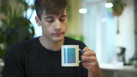 young european male student is enjoying his coffee or tea at the coffeehouse with natural background