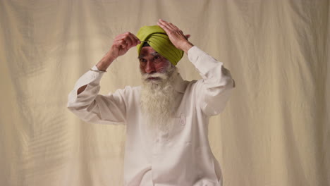 fotografía de estudio de un anciano sikh con barba atando tela para el turbante contra un fondo plano como secuencia parte 3 de 3