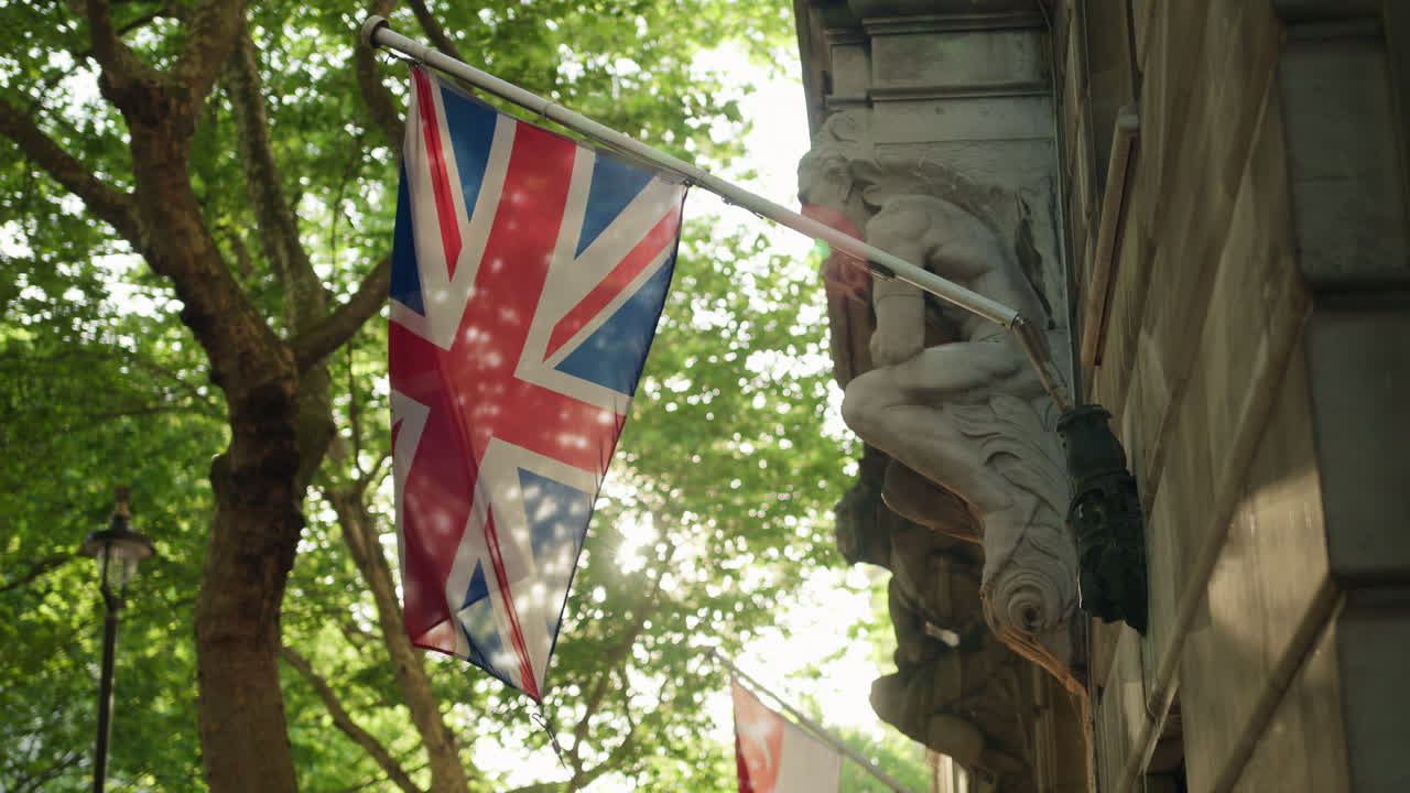 Union Jack flag hanging on a historic building with green trees on the background in London, England