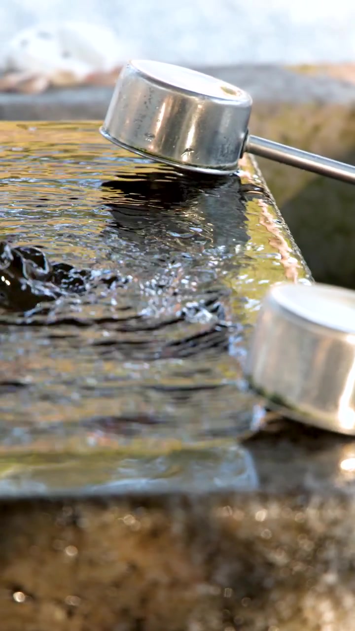 Primo piano di acqua che increspa in una vasca di pietra con mestoli di metallo al Santuario di Oyama