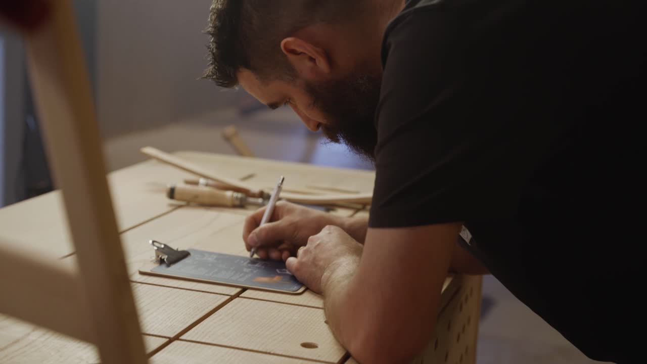 A craftsman leans over his workspace, sketching detailed woodworking plans in a studio workshop, symbolizing focus, creativity, and precision craftsmanship