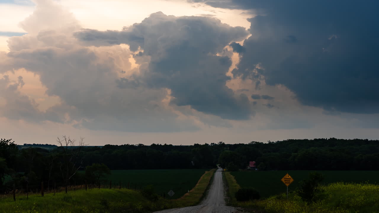 Country road leading away with dark clouds gently moving in the sky