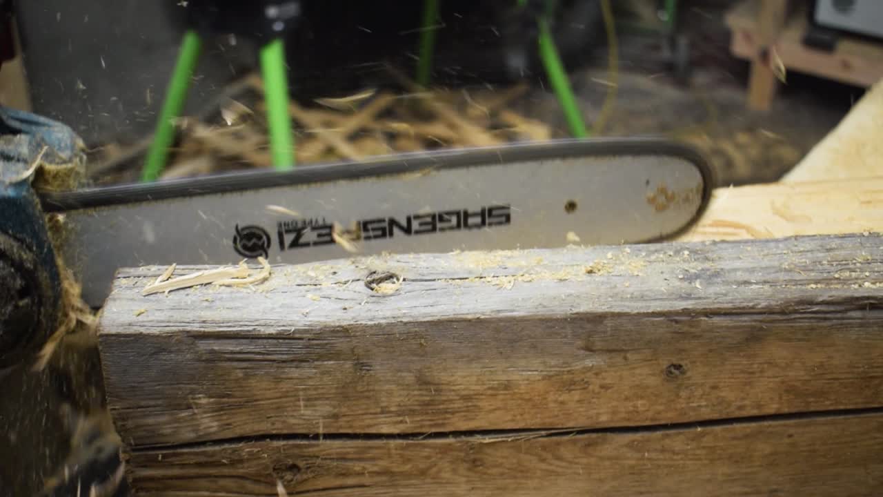 Close Up Of Professional Woodworker Work Piece Of Wood With Electric Chainsaw While Wood Chips Fly Around. slow motion - pan shot.