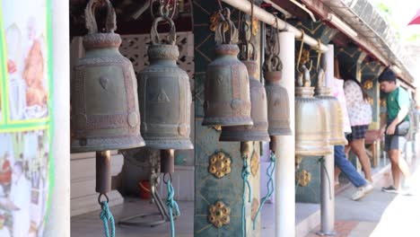 bells hanging at a temple with people walking by