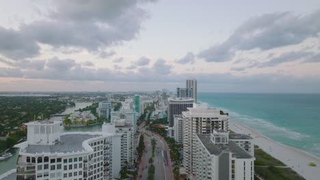 Landungsaufnahmen-Eines-Modernen-Stadtbezirks-An-Der-Meeresküste-In-Der-Abenddämmerung.-Reihe-Von-Luxuriösen-Mehrstöckigen-Apartmentgebäuden-Entlang-Der-Breiten-Straße.-Miami,-USA