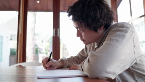 asian man writing idea plan on a notebook in a cafe