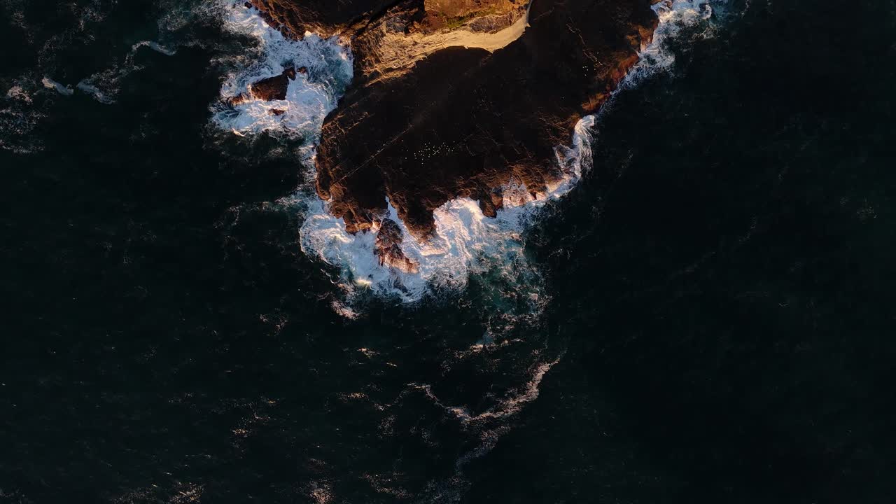 Aerial of crashing waves in dark ocean waters at golden hour dusk near Kiama coastline in Australia, natural backdrop background