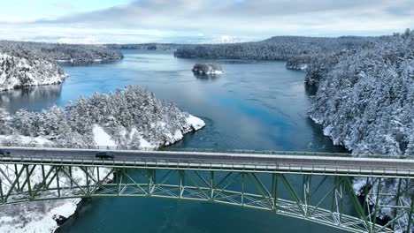 wide aerial view of a black car driving across deception pass bridge during the winter