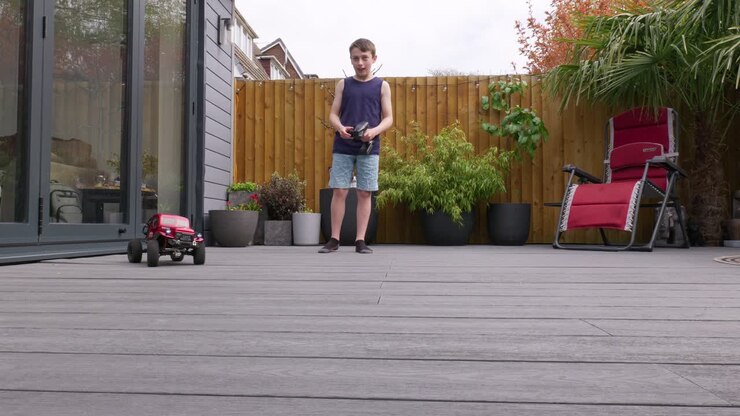 Giovane ragazzo a casa all'aperto in giardino che gioca con la sua auto RC, camion e 4x4.
