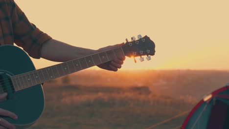 cerrar las manos del hombre con la guitarra en el campamento turístico al atardecer